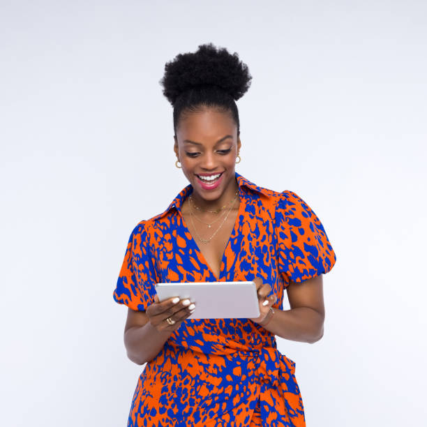 Happy young woman wearing animal pattern dress using digital tablet and smiling. Studio shot, white background.